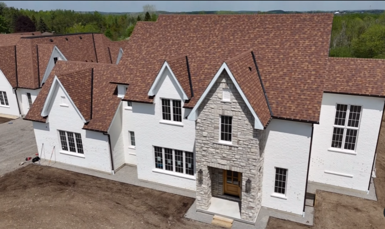 Modern white house with stone accent and brown shingle roof in suburban neighborhood.