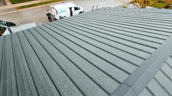 Metal roof installation in progress and workers in the background on a residential street.